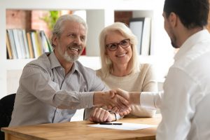 Happy old couple clients make financial deal handshake meeting lawyer